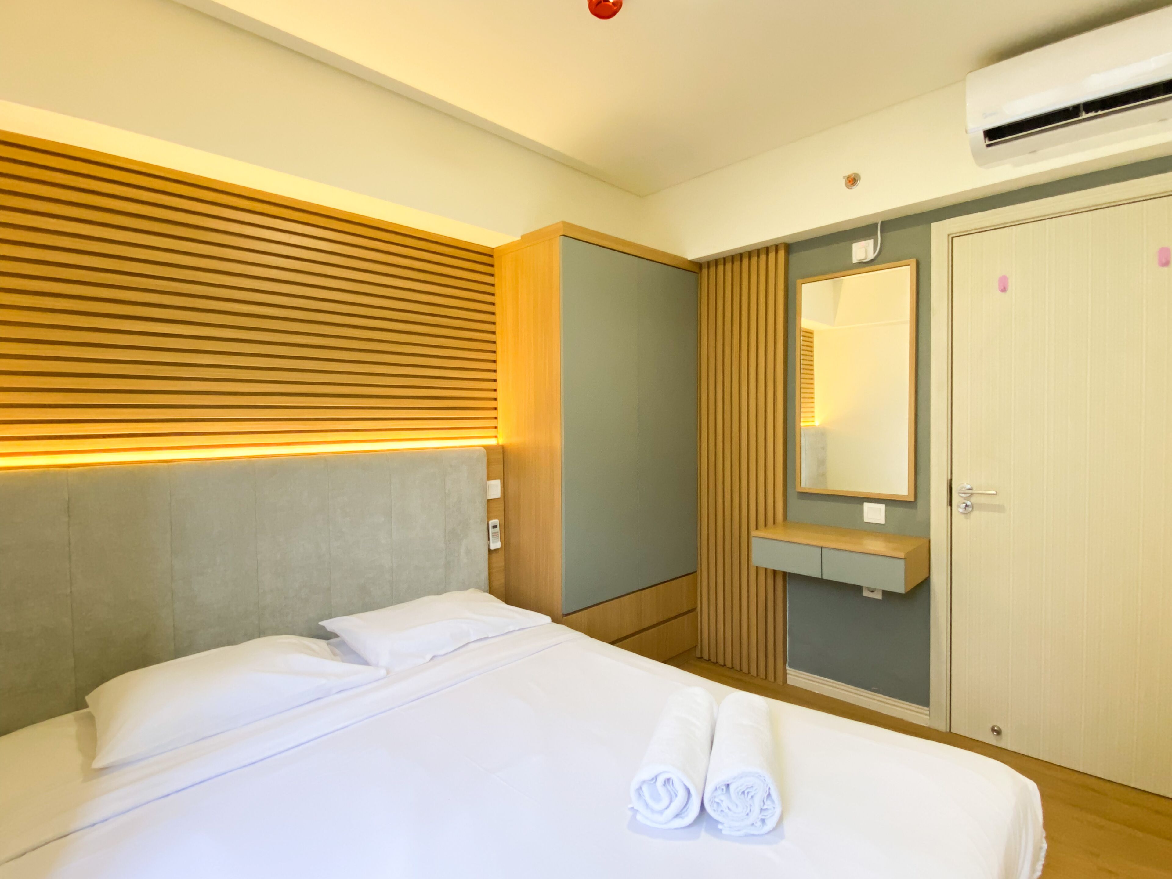 A hotel room with a bed, a wooden headboard, a built-in wardrobe, a mirror, and an air conditioning unit.