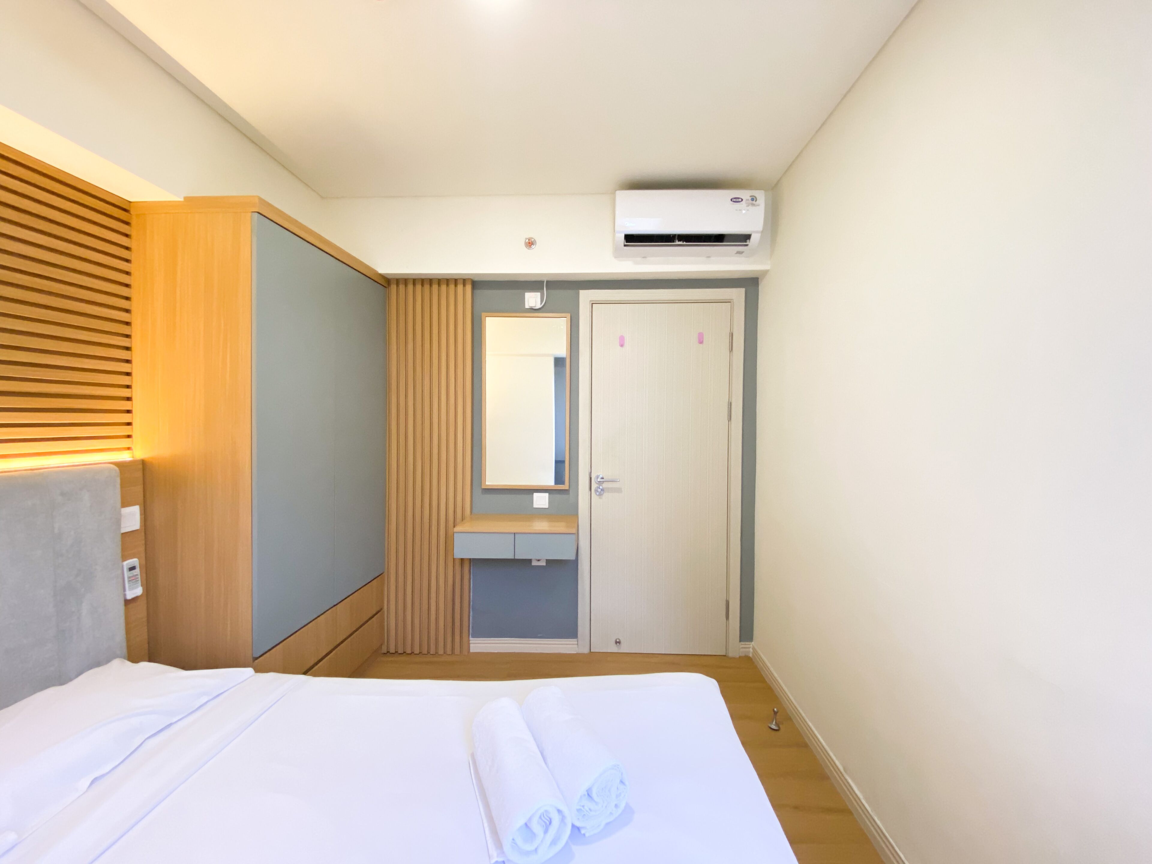 Una habitación de hotel con cama, cabecera de madera, armario empotrado, tocador con espejo y aire acondicionado.