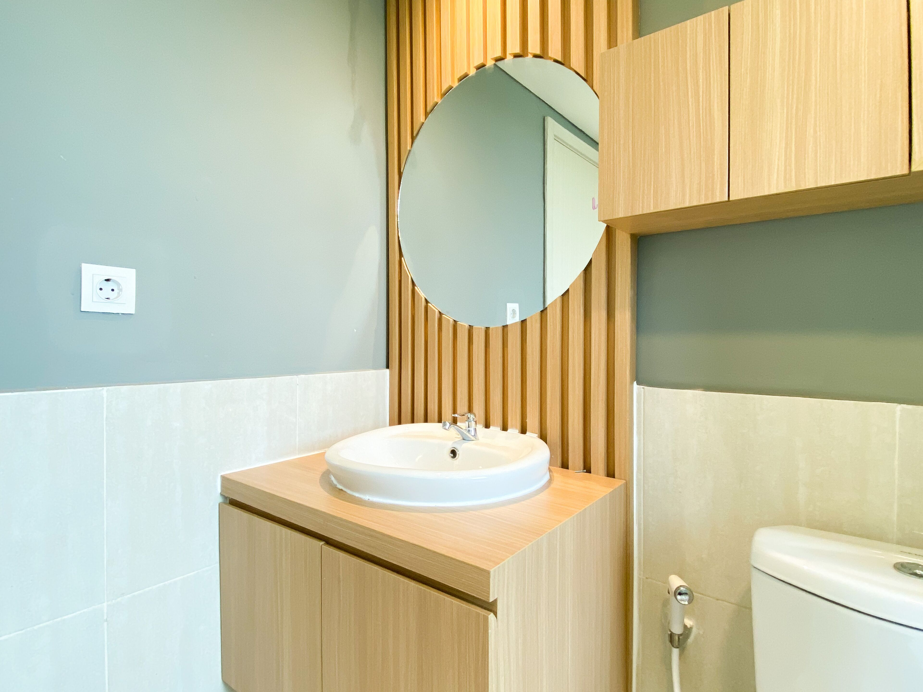 A modern bathroom with a wooden vanity, a round mirror, and a white sink.