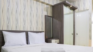 A neatly made bed with white linens and a folded towel, a wooden headboard, a nightstand with a mirror, and a wardrobe with a mirror.