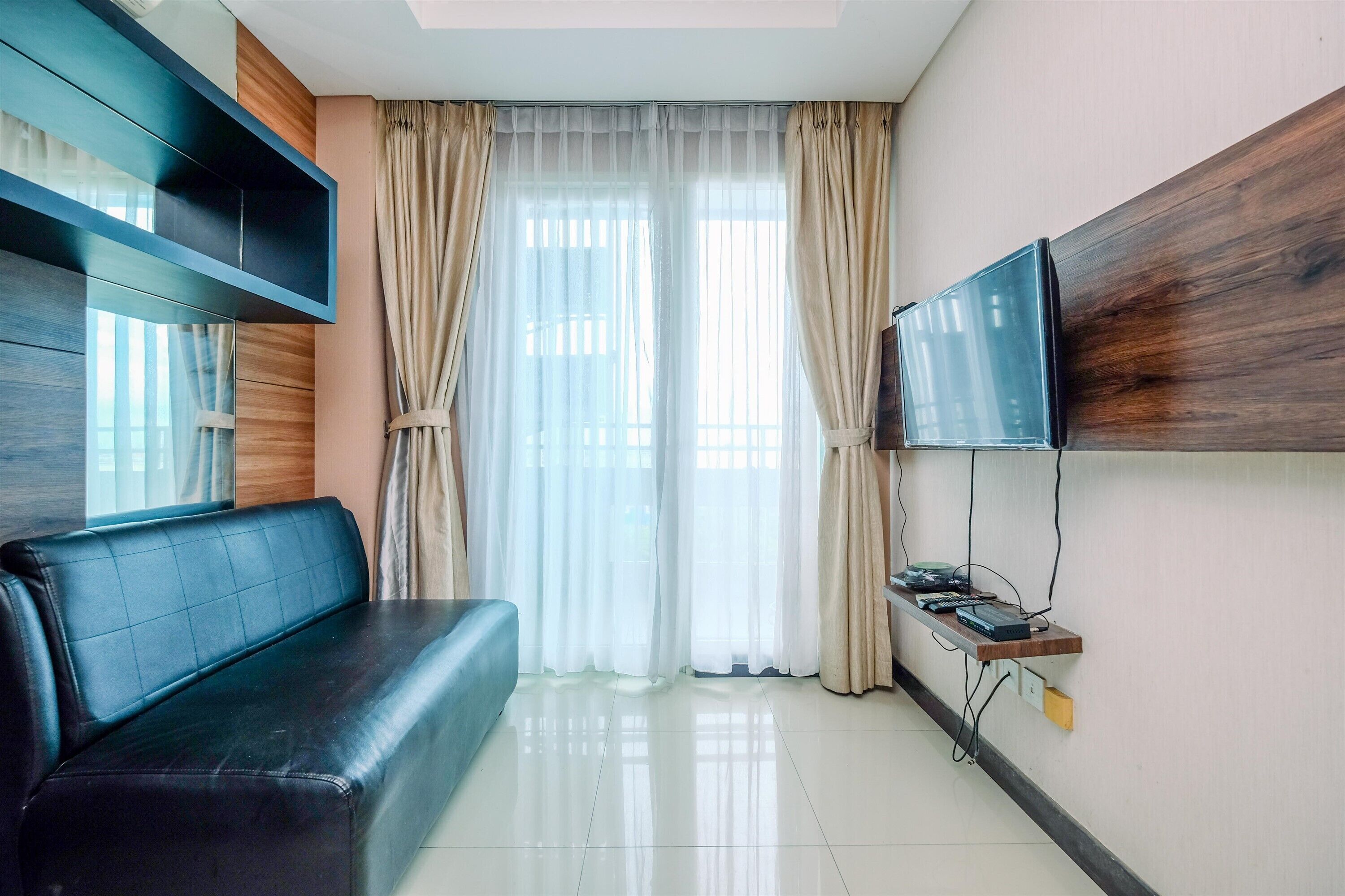 A modern living room with a black leather sofa, a mounted TV, and a wooden shelf with electronic devices.