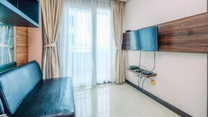 Ein modernes Wohnzimmer mit einer Couch, einem Wand-Fernseher und einem Fenster mit transparenten Vorhängen.