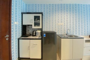 A compact kitchen with white cabinets, a black countertop, a stainless steel sink, and a refrigerator.