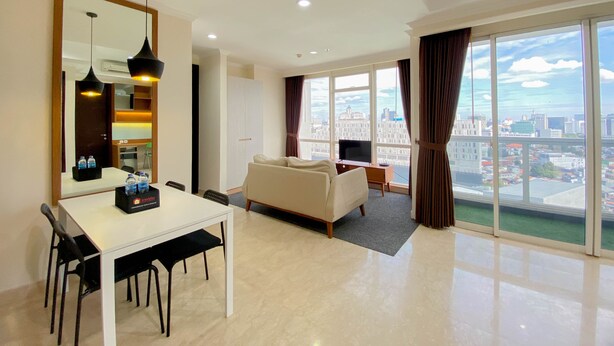 Ein modernes Wohnzimmer mit Sofa, Esstisch mit Stühlen, Fernseher und einem großen Fenster mit Vorhängen.