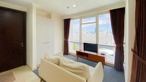Ein modernes Hotelzimmer mit großem Fenster, einer Couch, einem Fernseher und einem Holztischchen.