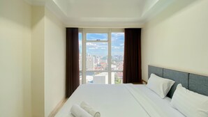 Ein Hotelzimmer mit einem großen Bett und Blick auf die Stadt durch ein Fenster, wobei sich die Skyline draußen erstreckt.