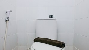 A toilet with a white tank and a brown towel on the seat, a white pipe, and a tiled wall. - Homey And Cozy Studio Room At Suites @Metro Apartment (Bandung)