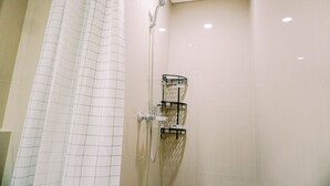 A shower with a grid-patterned curtain, a handheld showerhead, and a wall-mounted shelf with a basket. - Homey And Simply Look 1Br Bintaro Embarcadero Apartment (South Tangerang)