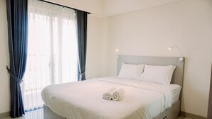 A neatly made bed with white linens and two rolled towels, a headboard, and a bedside lamp. - Homey And Simply Look 1Br Bintaro Embarcadero Apartment (South Tangerang)