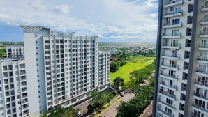 A high-rise residential building with multiple balconies and a view of a green park and distant cityscape. - Homey And Best Deal 1Br Casa De Parco Apartment (Pagedangan)