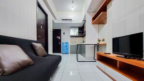 A modern living room with a black sofa, a wooden entertainment unit, and a flat-screen TV. - Homey And Best Deal 1Br Casa De Parco Apartment (Pagedangan)