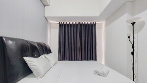 A modern hotel room with a large bed, a dark headboard, white bedding, and a curtain. - Homey And Best Deal 1Br Casa De Parco Apartment (Pagedangan)