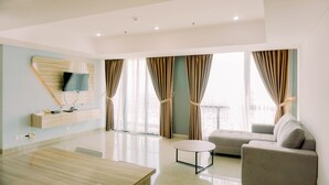 A modern living room with a sofa, a round coffee table, and a TV mounted on the wall. - Spacious And Elegant 2Br At 35Th Floor Hillcrest House Apartment (Curug)