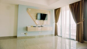 A modern living room with a flat-screen TV mounted on a wooden panel, a built-in cabinet below, and a large window with curtains. - Spacious And Elegant 2Br At 35Th Floor Hillcrest House Apartment (Curug)