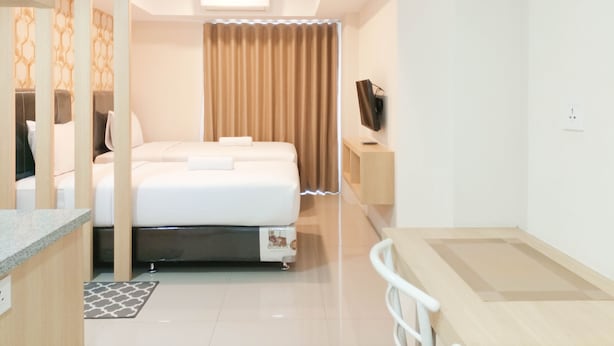 A hotel room with a bed, a TV on a stand, a desk, and a window with curtains.