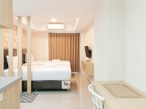 Une chambre d’hôtel avec un lit, un téléviseur posé sur un meuble, un bureau et une fenêtre avec des rideaux.