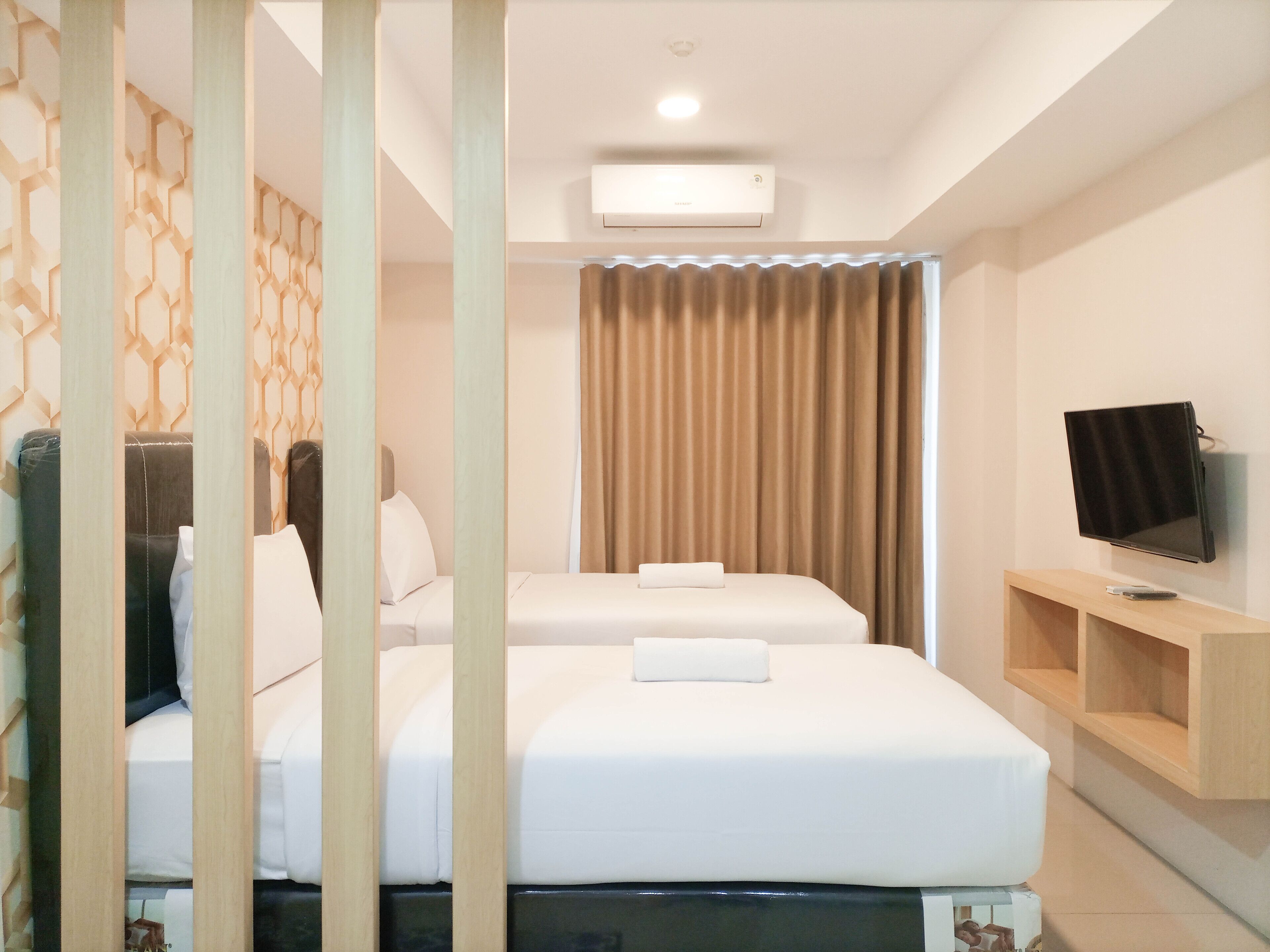A hotel room with two beds, a television on a wooden stand, and a curtain.