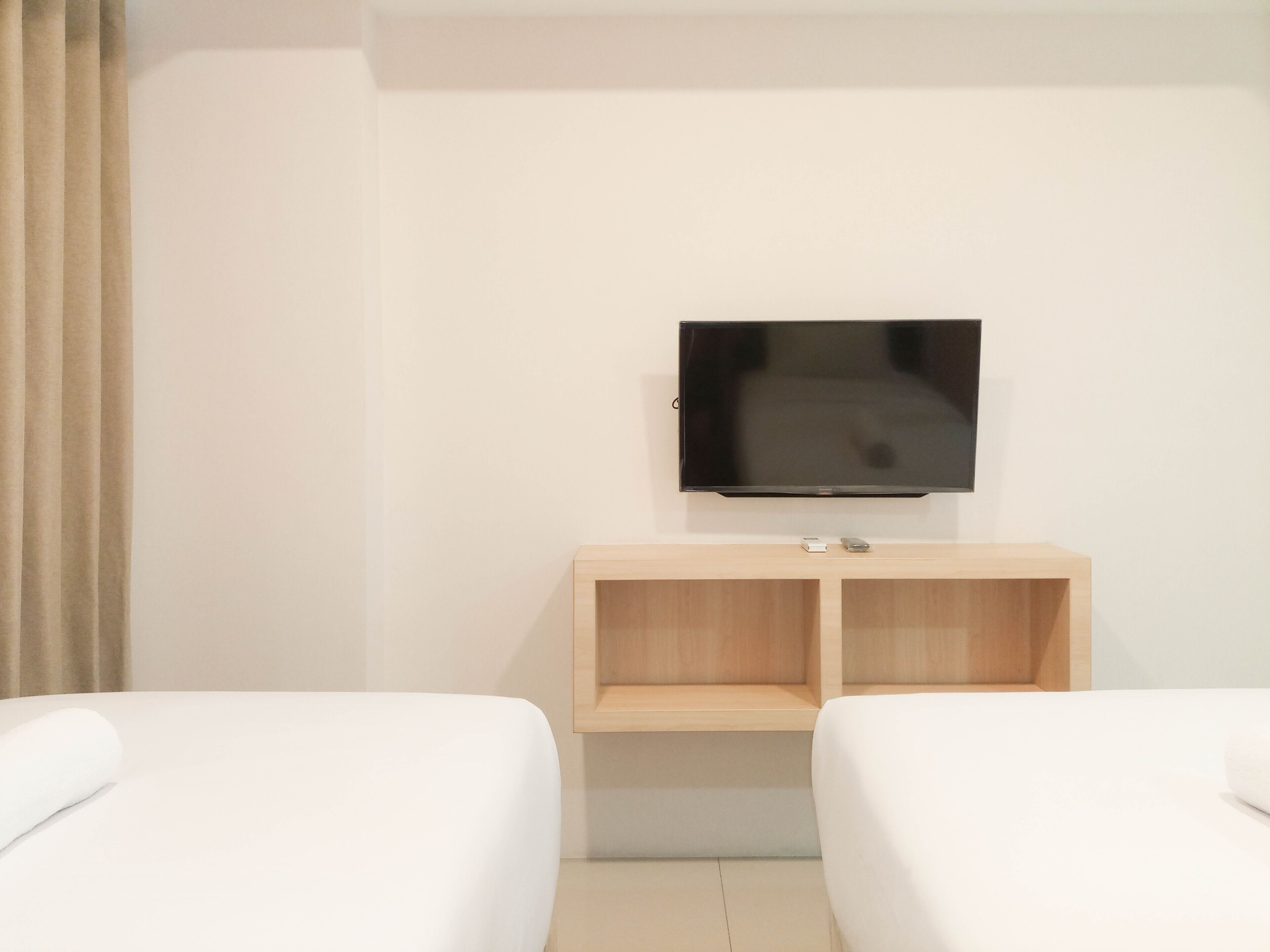 Quarto de hotel com duas camas, uma televisão fixada na parede e um armário de madeira abaixo.