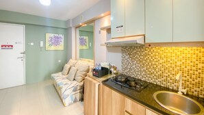 A compact kitchen with a sink, stove, and a microwave on the countertop. There is a sofa with cushions in the adjacent living area. - Best Strategic 2Br Apartment At Bassura City (Jakarta)