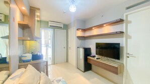 A modern living room with a sofa, a flat-screen TV, a built-in kitchen area, and a door. - Best Strategic 2Br Apartment At Bassura City (Jakarta)