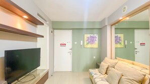 A living room with a flat-screen TV, a sofa, and a large mirror. - Best Strategic 2Br Apartment At Bassura City (Jakarta)