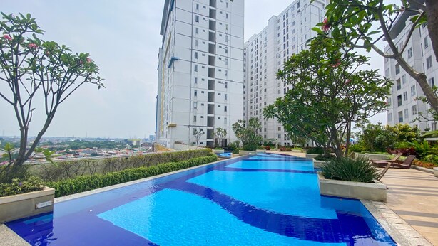 A rooftop swimming pool with clear blue water, surrounded by greenery and tall residential buildings. - Best Strategic 2Br Apartment At Bassura City (Jakarta)