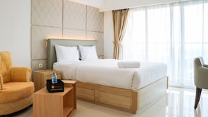 A modern hotel room with a large bed, a wooden nightstand, a chair, and a view of the city through large windows.