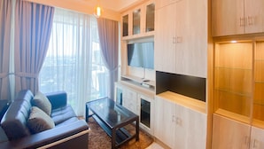 A modern living room with a sofa, a glass coffee table, and built-in wooden cabinets. - Nice And Elegant 2Br At Menteng Park Apartment (Jakarta)