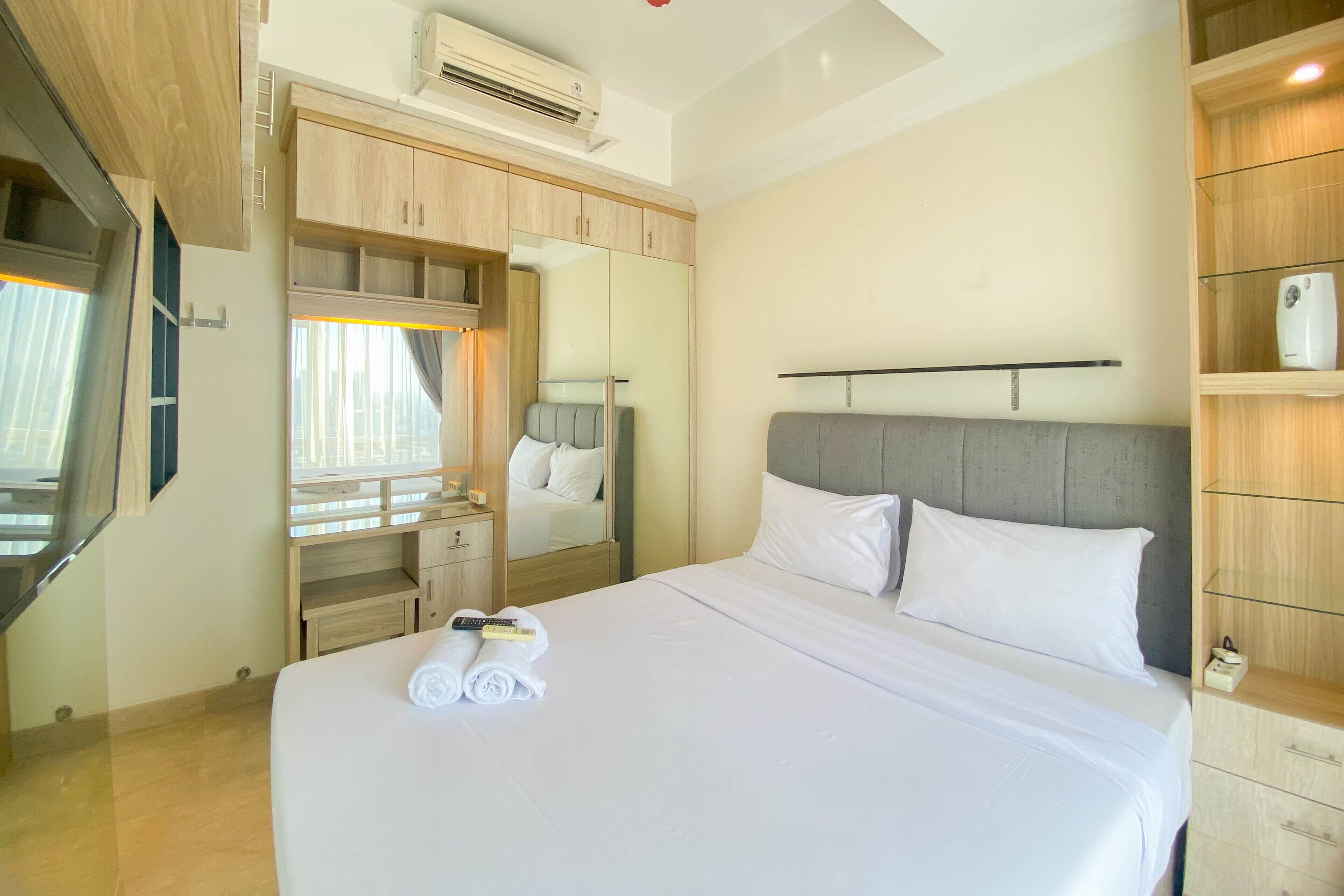 A hotel room with a large bed, a wardrobe with a mirror, a vanity with a mirror, and a TV mounted on the wall.