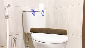 A white toilet with a brown toilet paper holder and a visible toilet paper roll. - Good Deal And Homey Studio At 11St Floor Citra Living Apartment (Jakarta)