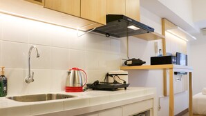 A modern kitchen with a stainless steel sink, a kettle, a portable stove, and a microwave on a shelf. - Modern Studio Room At Tokyo Riverside Pik 2 Apartment (Teluknaga)