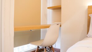 A room with a bed, a white chair, and wooden shelves against the wall. - Modern Studio Room At Tokyo Riverside Pik 2 Apartment (Teluknaga)