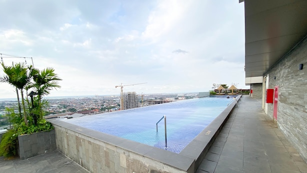 Piscina infinita en la azotea con vistas a la ciudad y grúas de construcción.