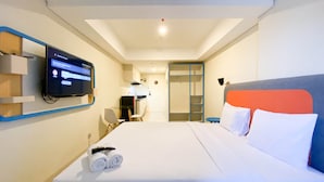 Habitación de hotel con cama, televisión montada en la pared, escritorio con silla y armario.