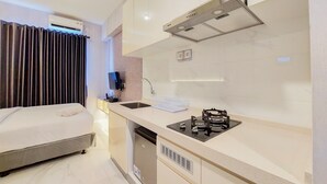 A compact hotel room with a kitchenette, a bed, a TV, and a window with curtains. - Restful And Best Choice Studio Sky House Bsd Apartment (Pagedangan)