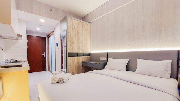 A modern hotel room with a large bed, a bedside table, a built-in wardrobe, and a small kitchenette. - Restful And Best Choice Studio Sky House Bsd Apartment (Pagedangan)