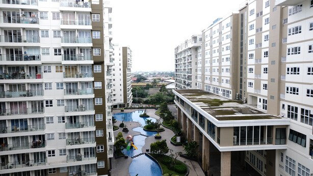 A high-rise residential building with multiple balconies, a central courtyard with a water feature, and a view of the surrounding area. - Homey Studio Room At 7Th Floor Gateway Pasteur Apartment (Cimahi)