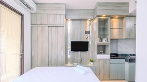 A modern hotel room with a large bed, a flat-screen TV, a small kitchen area with a sink and a marble countertop, and wooden cabinetry. - Cozy Stay Studio At Transpark Cibubur Apartment (Bekasi)