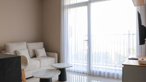 A modern living room with a sofa, two small tables, a TV, and a balcony with sheer curtains. - Wonderful And Homey 1Br Ciputra International Apartment (Jakarta)