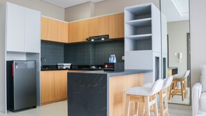 A modern kitchen with wooden cabinets, a black countertop, and a built-in island with bar stools. - Wonderful And Homey 1Br Ciputra International Apartment (Jakarta)