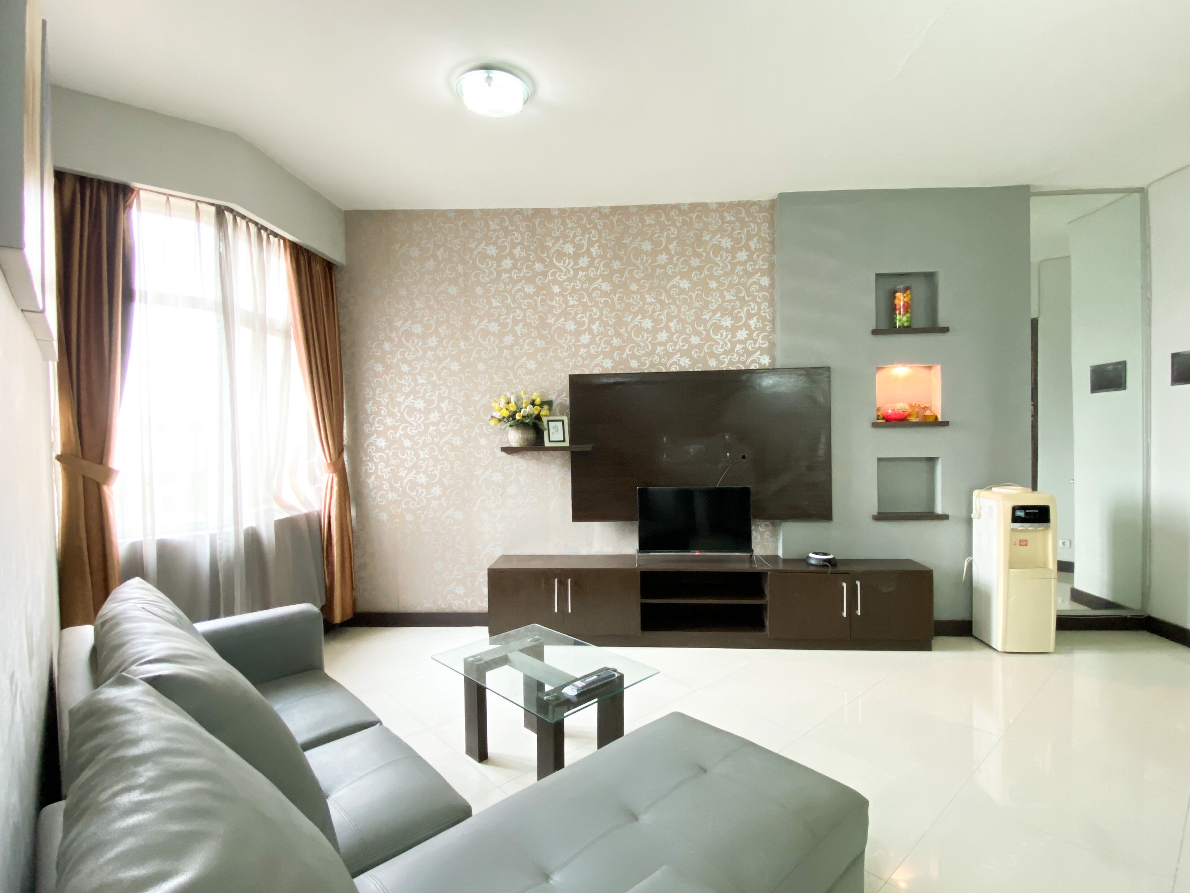 A modern living room with a sofa, a glass coffee table, a flat-screen TV on a wooden cabinet, and a water dispenser.