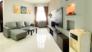 Un salón moderno con un sofá gris, una mesa de centro de cristal, un televisor de pantalla plana y una cocina integrada con cafetera.