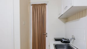 A kitchen with a sink, a faucet, a cabinet, and a door with a curtain.