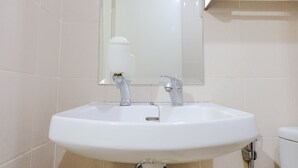 A white bathroom sink with two faucets, a mirror above it, and a toilet to the right.