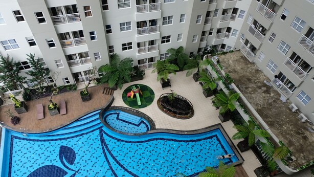 A high-rise building with a rooftop swimming pool, surrounded by greenery and a small playground.