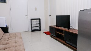 A bedroom with a bed, a TV, a refrigerator, a black cabinet, and a white door.