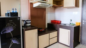 A compact kitchen with a refrigerator, a microwave, a sink, and a stove. There are cabinets and a countertop with various items. - Homey 2Br At Suites @Metro Apartment (Bandung)