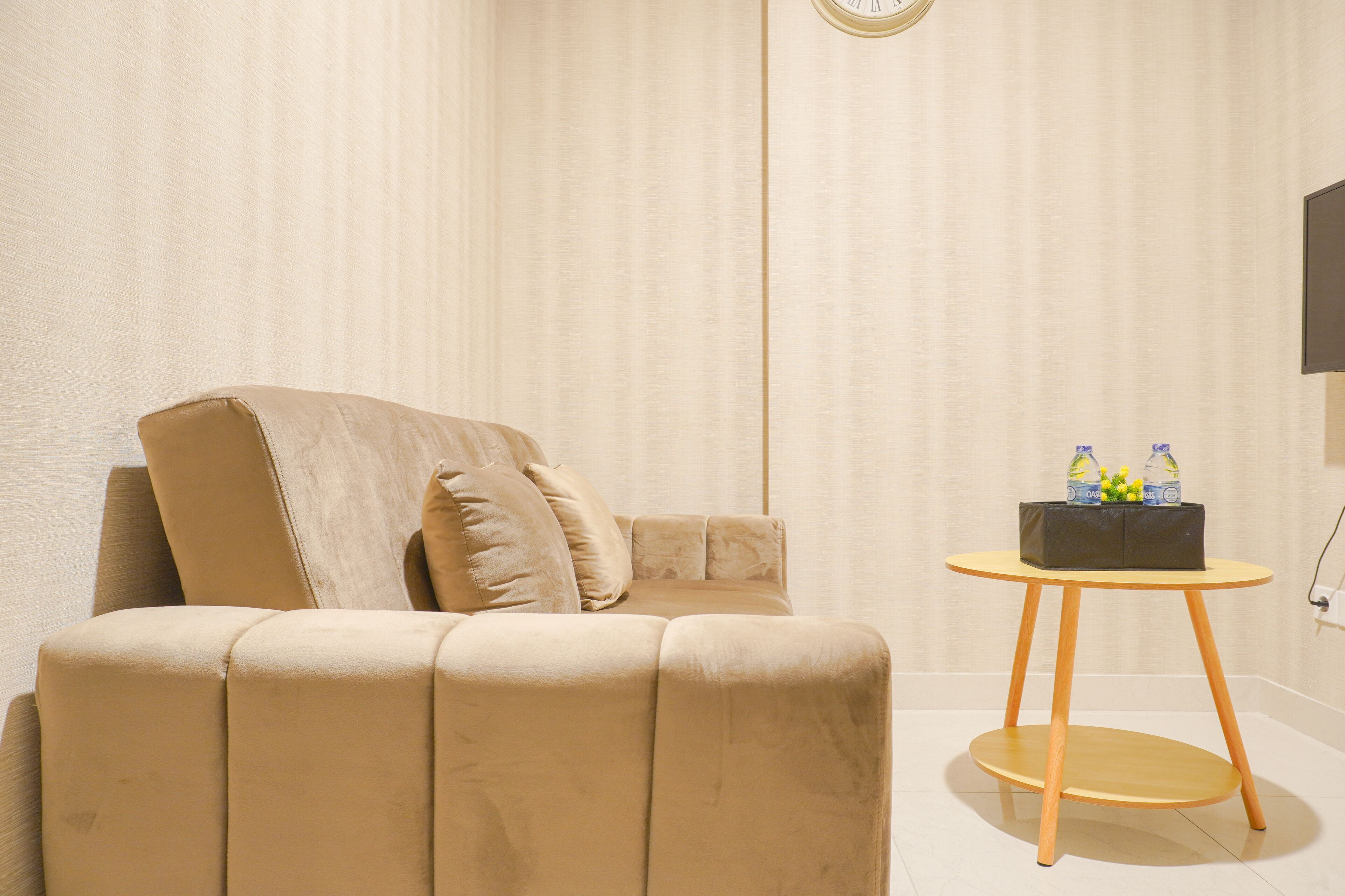 A modern room with a beige sofa, a small round wooden table, and a wall-mounted TV.