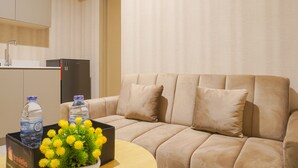 A modern hotel room with a beige sofa, a small wooden table, and a black box containing water bottles and yellow flowers. - Modern Look 1Br With Golf Island And Sea View Gold Coast Apartment (Jakarta)