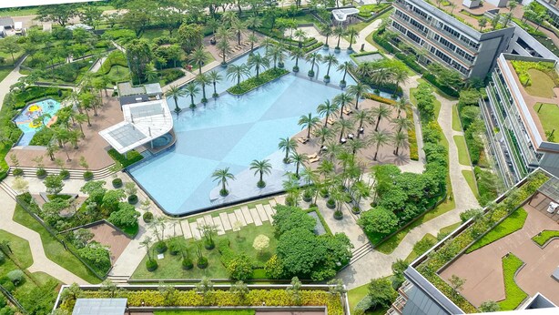 An aerial view of a modern hotel with a large central pool surrounded by palm trees and greenery, a children's play area, and a contemporary building with multiple floors. - Modern Look 1Br With Golf Island And Sea View Gold Coast Apartment (Jakarta)